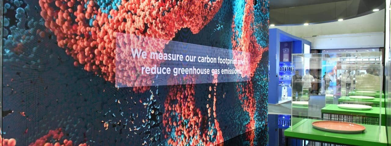 We are measuring our carbon footprint and reducing greenhouse gas emissions” written on the exhibitor stand glass wall